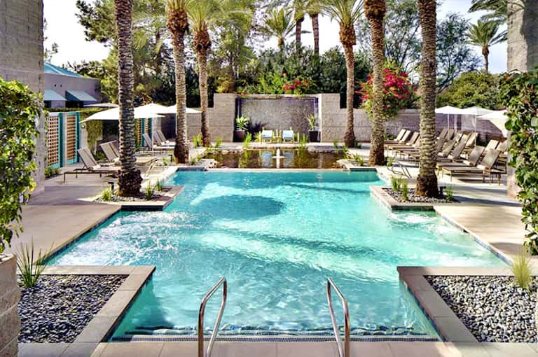 Luxury resort pool with turquoise water, palm trees, loungers, and modern concrete architecture