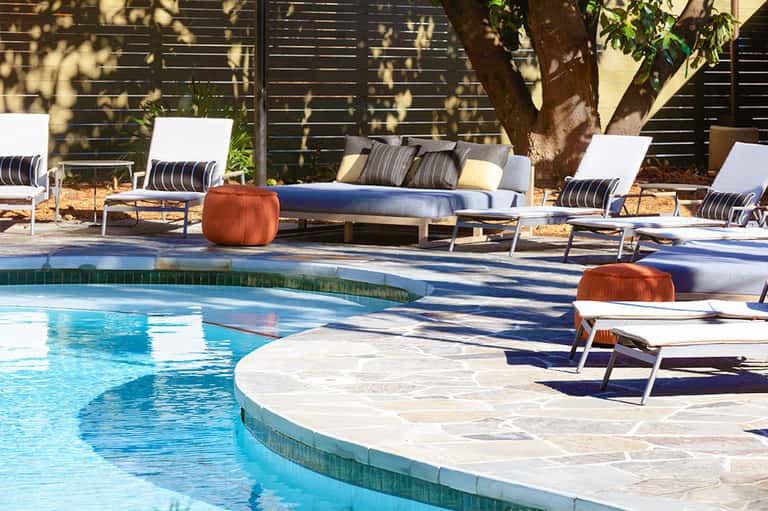 Modern resort pool with lounge chairs, daybed, and tree shade by contemporary building