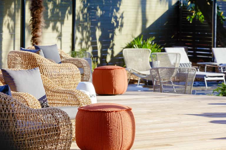 Woven lounge chairs and orange poufs on sunny wooden deck with white modern architecture