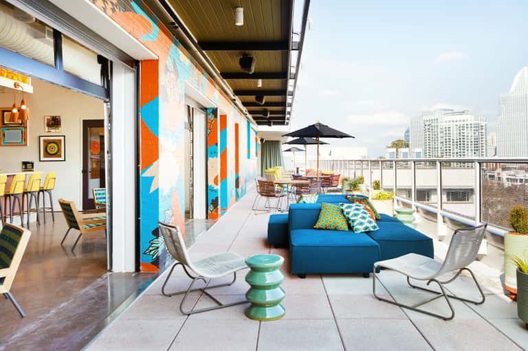 Colorful rooftop terrace with blue seating, orange and blue wall art, city views