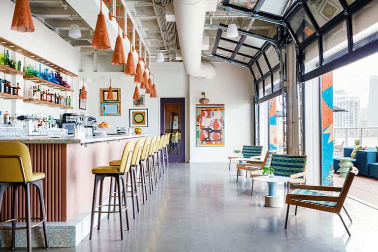 Contemporary bar and lounge space with orange pendant lights, colorful artwork, and floor-to-ceiling windows