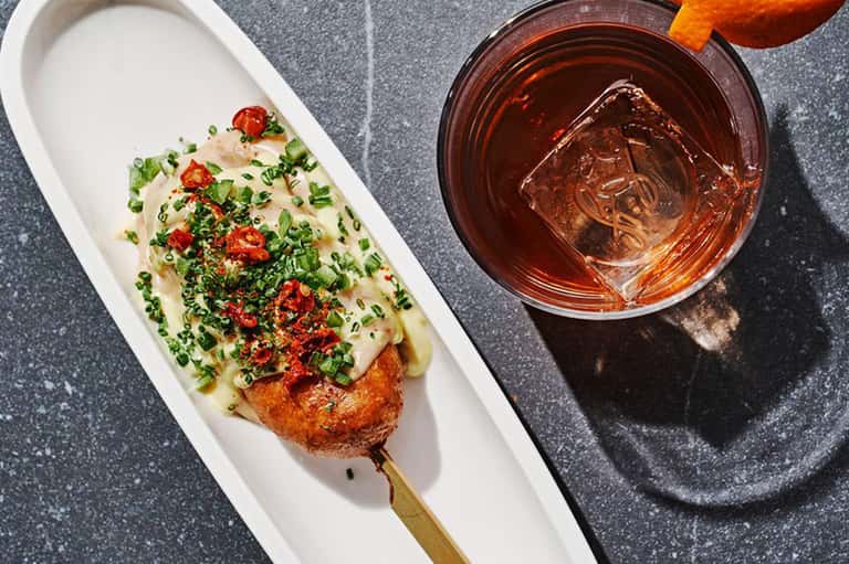 Gourmet appetizer on white plate with scallions and spiced sauce, tropical drink beside