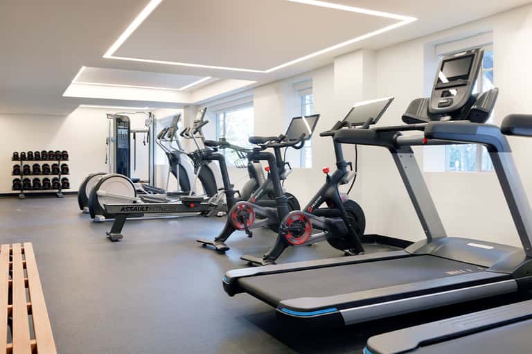 Modern fitness center with treadmills, exercise bikes, and dumbbells under geometric ceiling lights