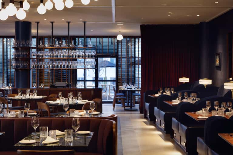 Upscale restaurant dining room with dark wood tables, modern bar, and ocean views