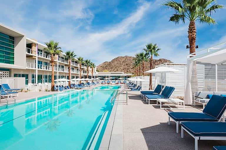 Resort pool deck with turquoise water, lounge chairs, palm trees, and desert mountain backdrop