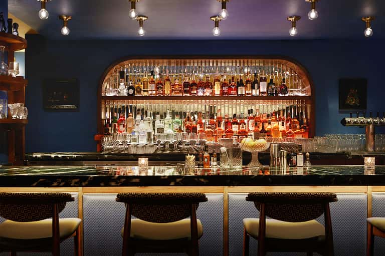 Upscale bar interior with brass-framed shelving, stocked bottles, pendant lighting, and modern seating