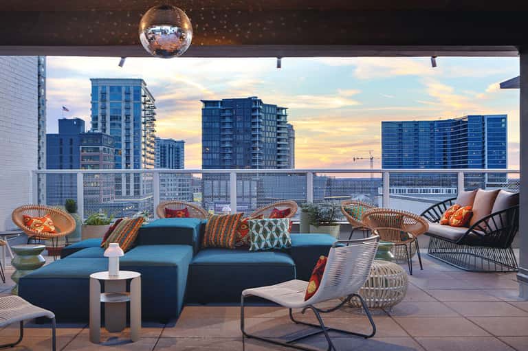 Modern rooftop lounge with blue seating, wicker chairs, and cityscape views at sunset with disco ball overhead