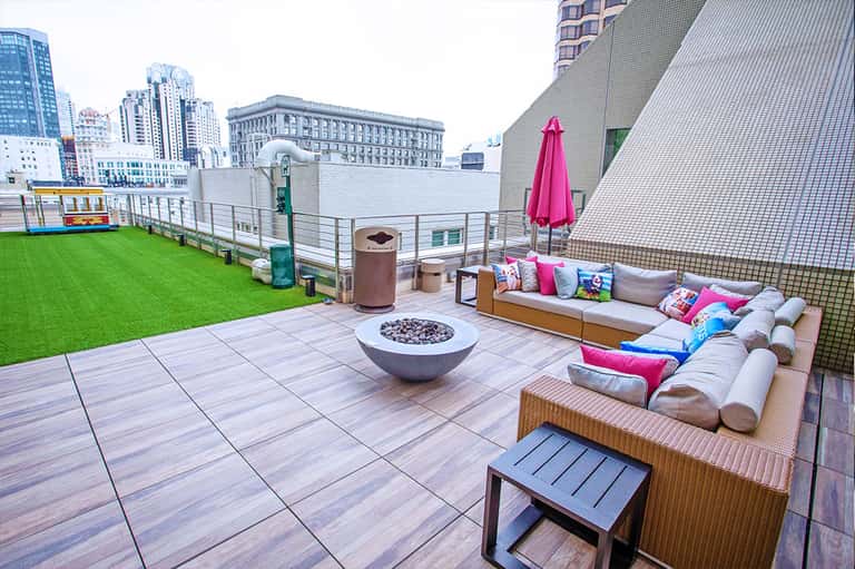 Rooftop terrace with artificial turf, fire pit, lounge seating, pink umbrella, and city skyline views