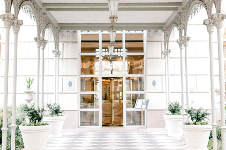 Elegant white colonnade entrance with ornate capitals leading to glass doors and potted plants