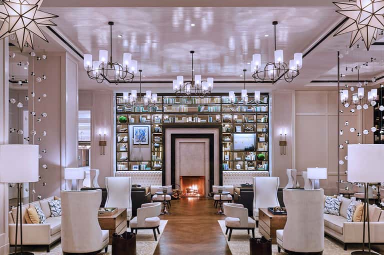Luxury lounge with symmetrical seating, fireplace, built-in bookshelves, and hanging crystal chandeliers