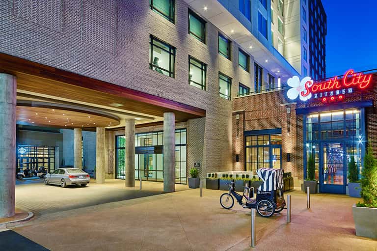 Modern urban hotel entrance with brick facade, South City Kitchen sign, and bicycle rickshaw at dusk