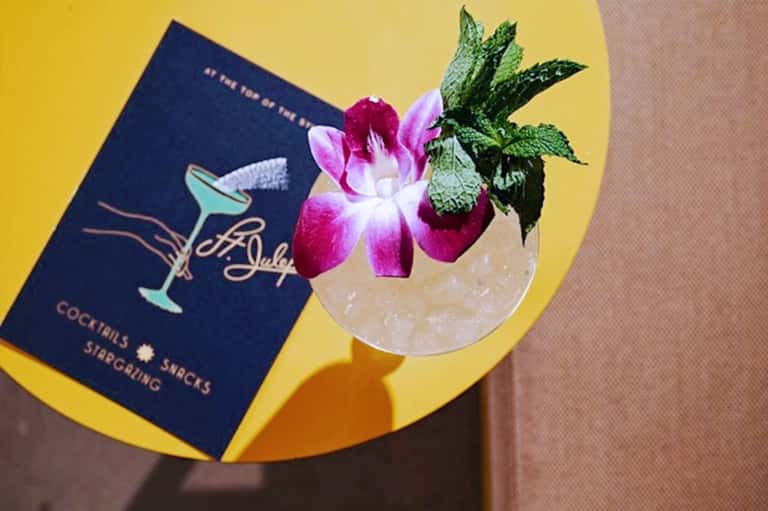 Tropical cocktail with orchid and mint garnish next to cocktail book on yellow table