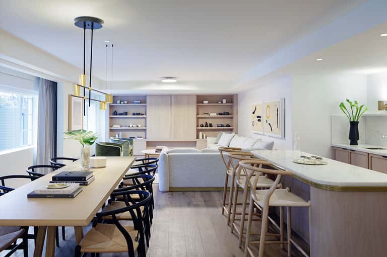 Modern open-concept living space with dining table, kitchen bar, sofa, and built-in shelving