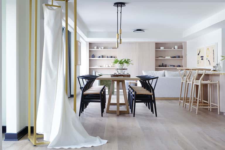 Modern dining room with light wood furniture, black wishbone chairs, white shelving, and floor-to-ceiling windows