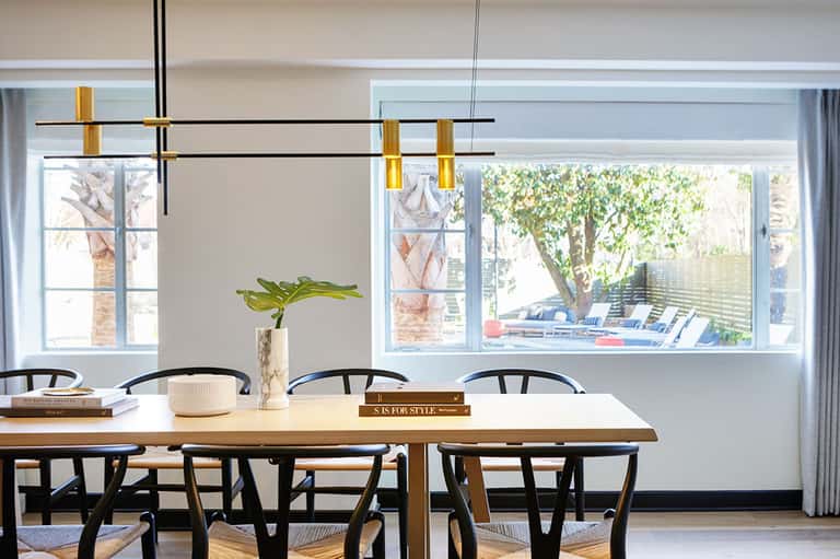 Modern dining room with wooden table, black chairs, and large windows overlooking palm trees