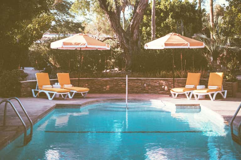 Resort pool with orange and white umbrellas, lounge chairs, and lush trees