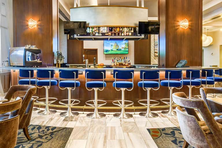 Elegant hotel bar with blue leather bar stools, brass accents, wood paneling, and illuminated wall sconces