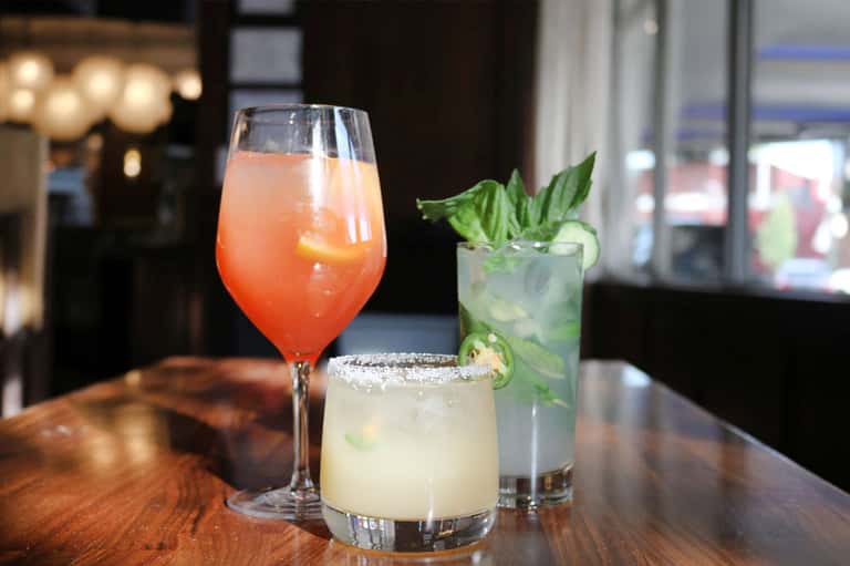Three colorful cocktails on a bar counter with elegant glassware