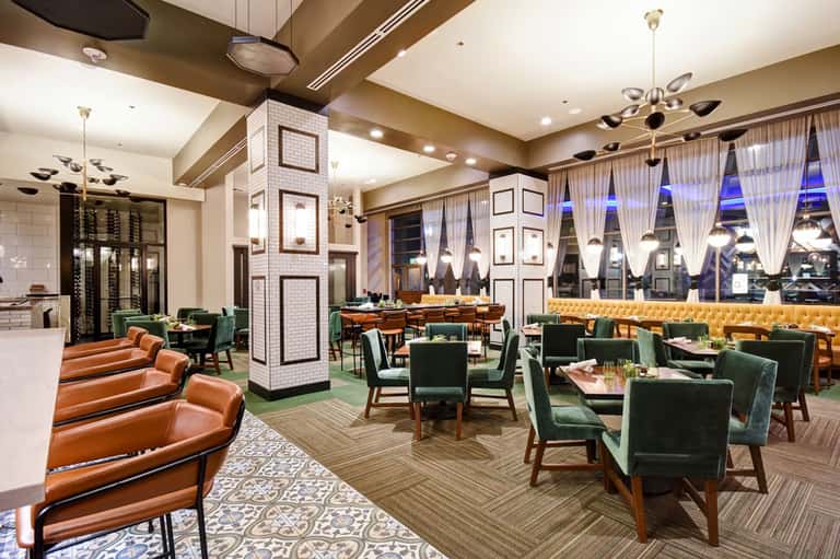 Modern upscale restaurant dining room with green chairs, orange lounge seating, and floor-to-ceiling windows