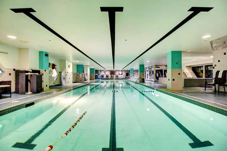 Indoor Olympic-length swimming pool with lane dividers and modern ceiling architecture in turquoise and white