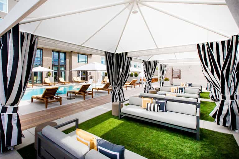 Modern rooftop pool deck with striped cabanas, loungers, and white tent canopies overlooking a building