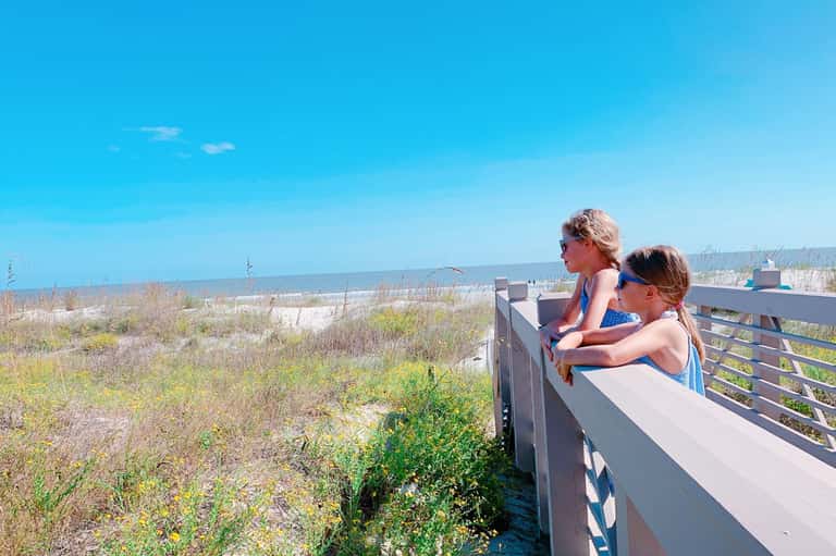 Two children on wooden beach boardwalk overlook dunes and ocean under clear blue sky
