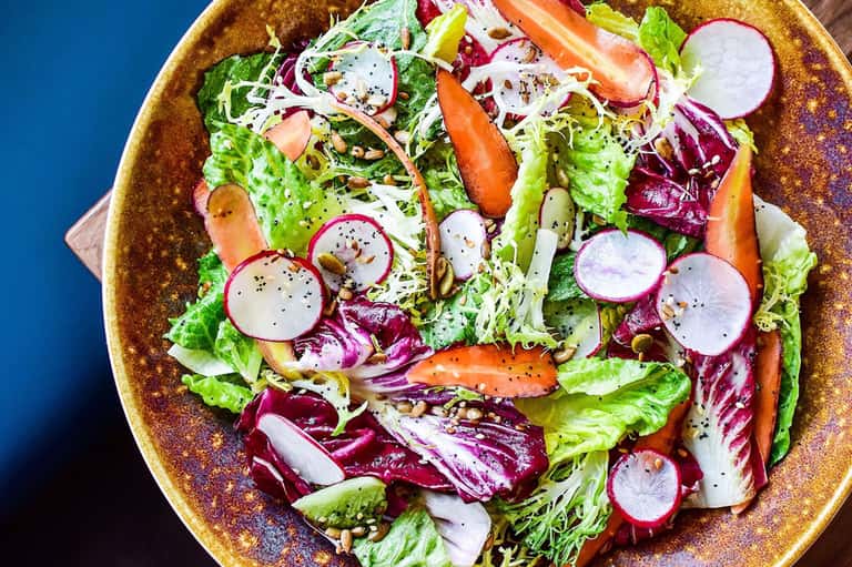 Colorful fresh salad with mixed greens, radishes, carrots, and seeds in a gold-rimmed bowl
