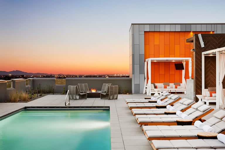 Rooftop pool deck at sunset with orange cabanas, lounge chairs, and city skyline view