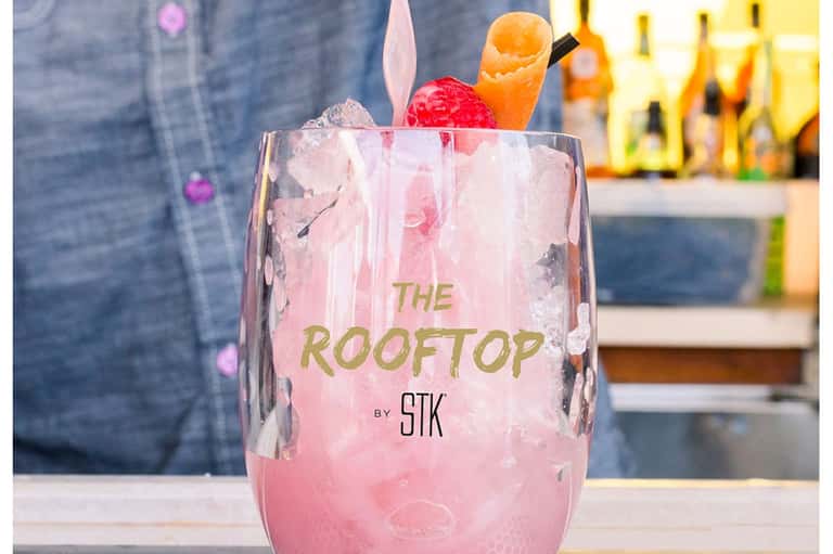 Pink cocktail drink with ice and fruit garnish labeled 'The Rooftop by STK' at a bar