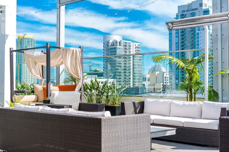 Luxury rooftop lounge with rattan furniture, sheer curtains, potted plants, and city skyline views