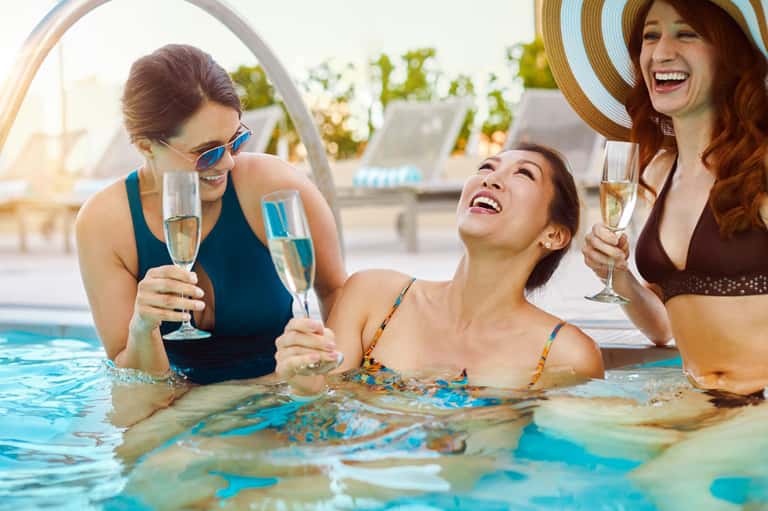 Three women celebrating with champagne glasses in swimming pool