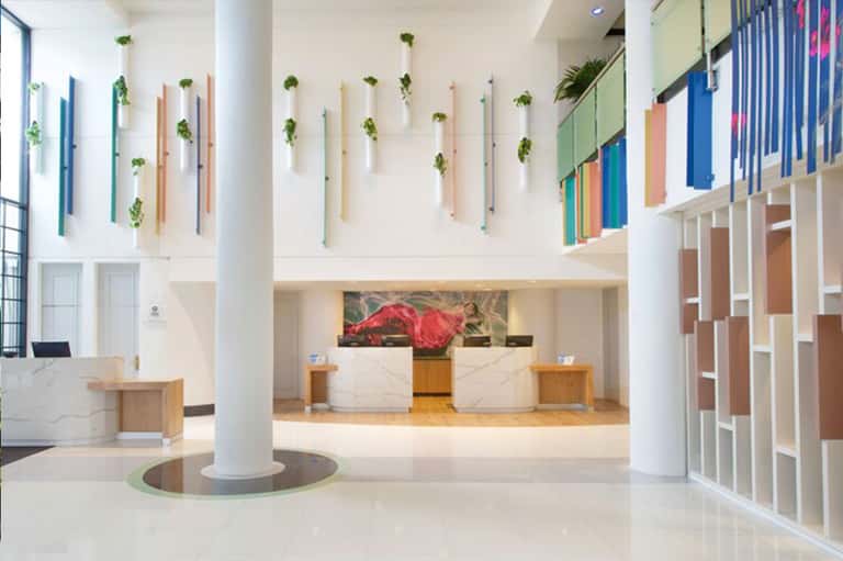 Modern hotel lobby with white marble reception desk, colorful wall plants, and hanging greenery