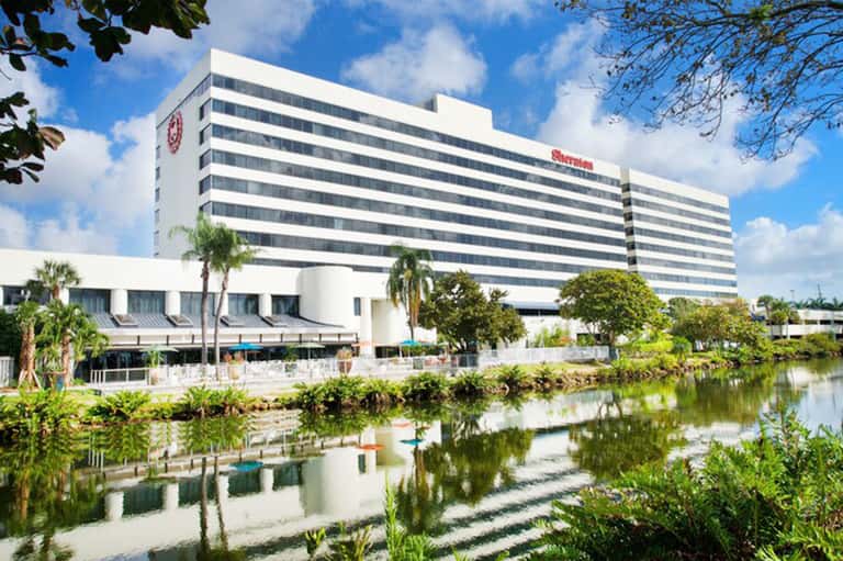 Modern waterfront hotel with white facade and striped windows, reflected in calm canal waters