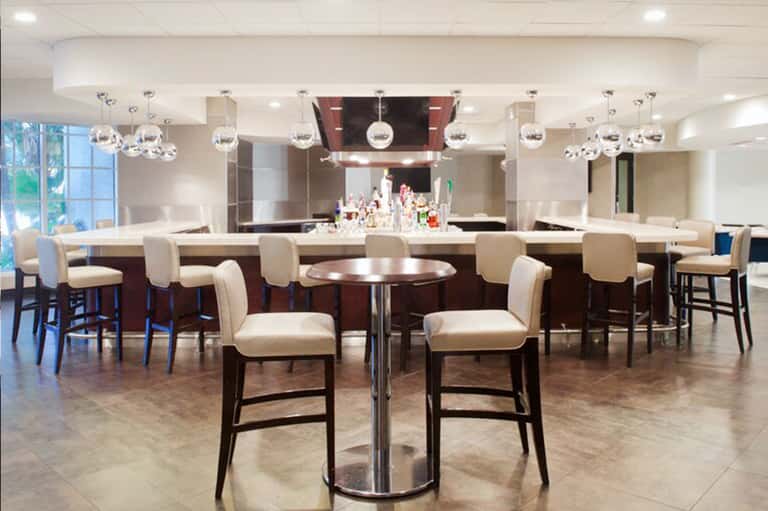Modern bar and lounge area with dark wood counter, pendant lighting, and cream-colored bar stools