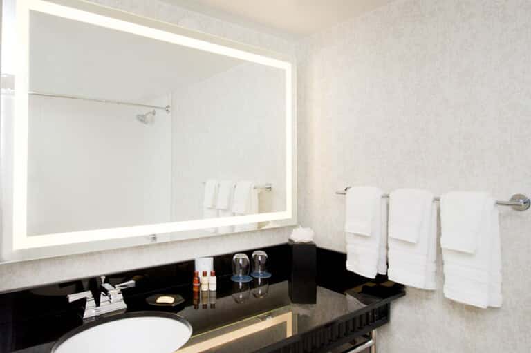Luxury bathroom vanity with illuminated mirror, black countertop, and white towels