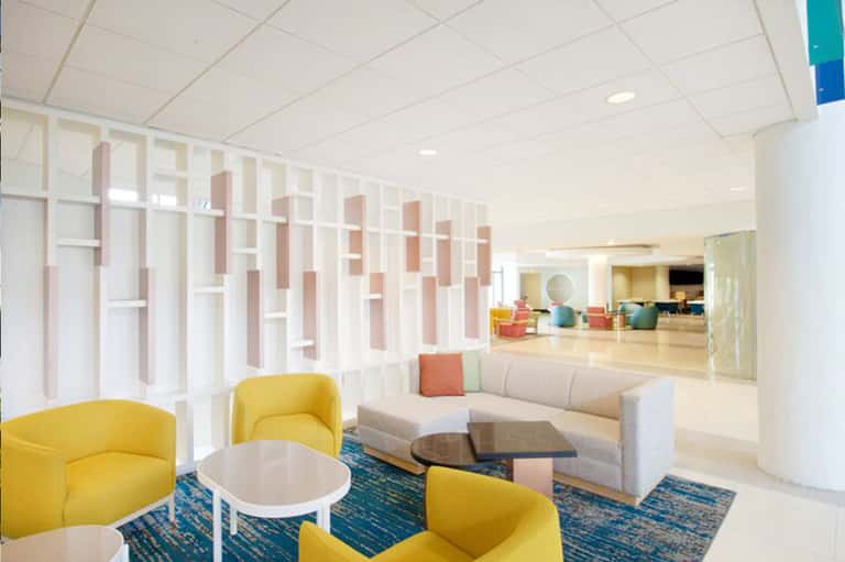 Modern hotel lobby lounge with yellow accent chairs, beige sofa, and geometric wall shelving