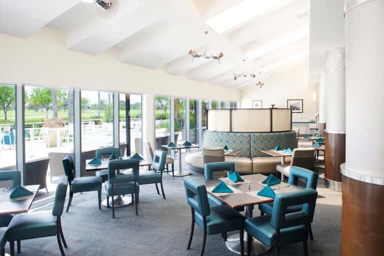 Bright modern dining area with teal chairs, wooden tables, and large windows overlooking grounds