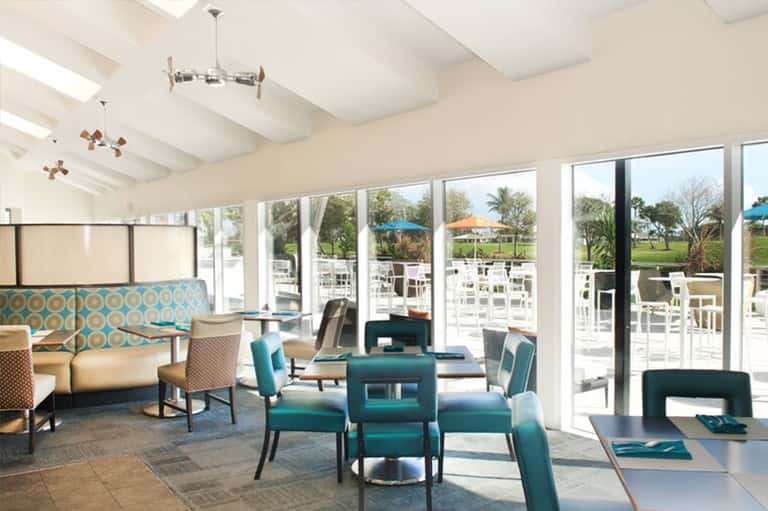Bright modern lounge with turquoise seating, large windows overlooking outdoor patio and golf course