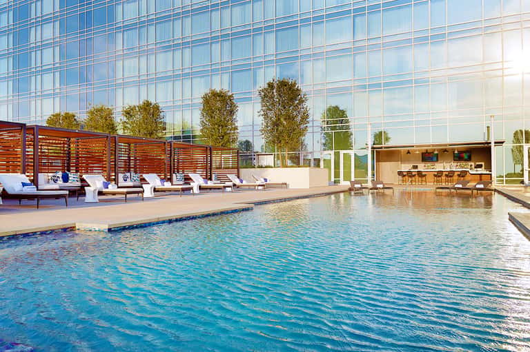 Modern indoor pool with loungers, wooden privacy screens, bar area, and glass building