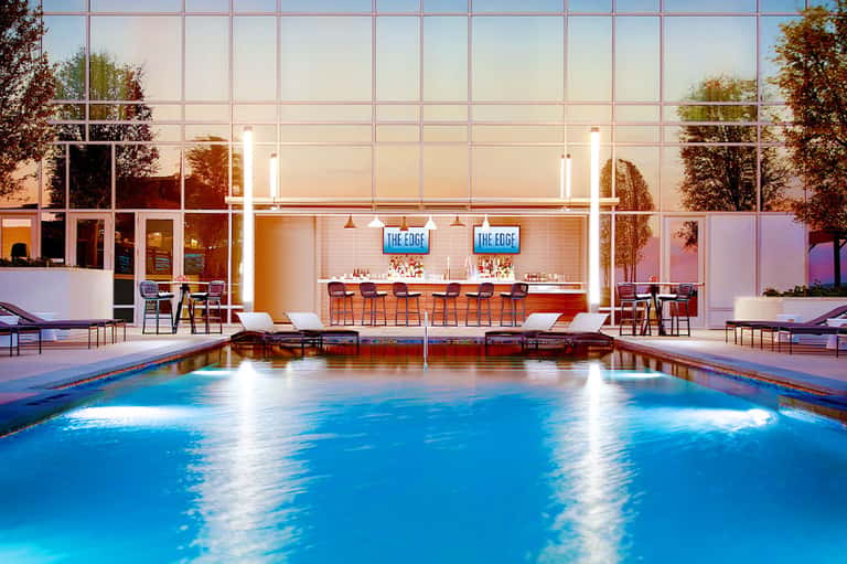 Modern indoor lap pool with floor-to-ceiling windows, bar area, and contemporary lounge seating