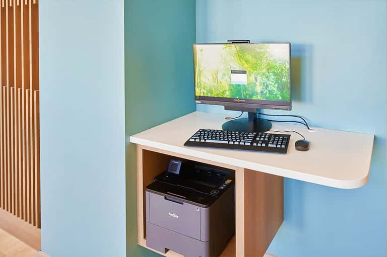 Modern workspace with desktop computer, keyboard, mouse, and printer on light wood desk against blue wall