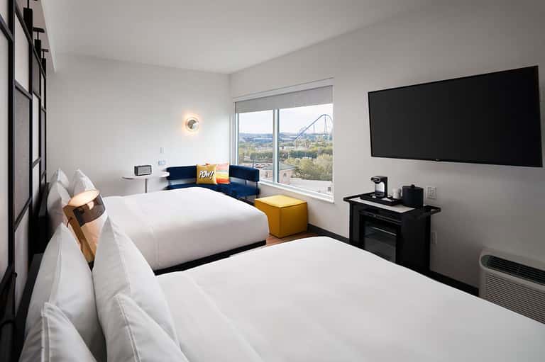 Modern hotel room with two beds, ocean view, blue accent chairs, and flat-screen TV