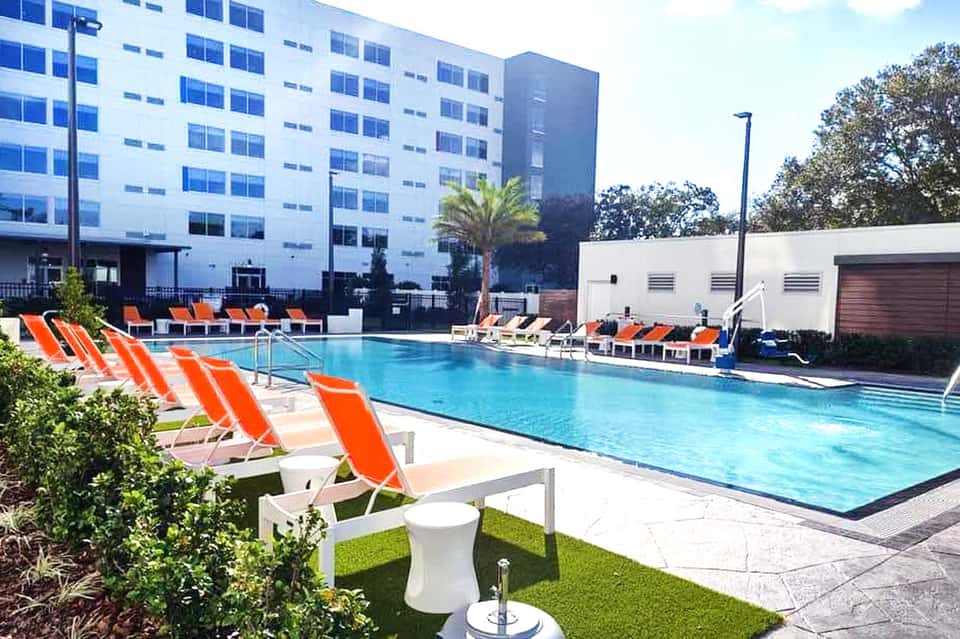 Resort pool with bright orange lounge chairs and white building with palm trees in background