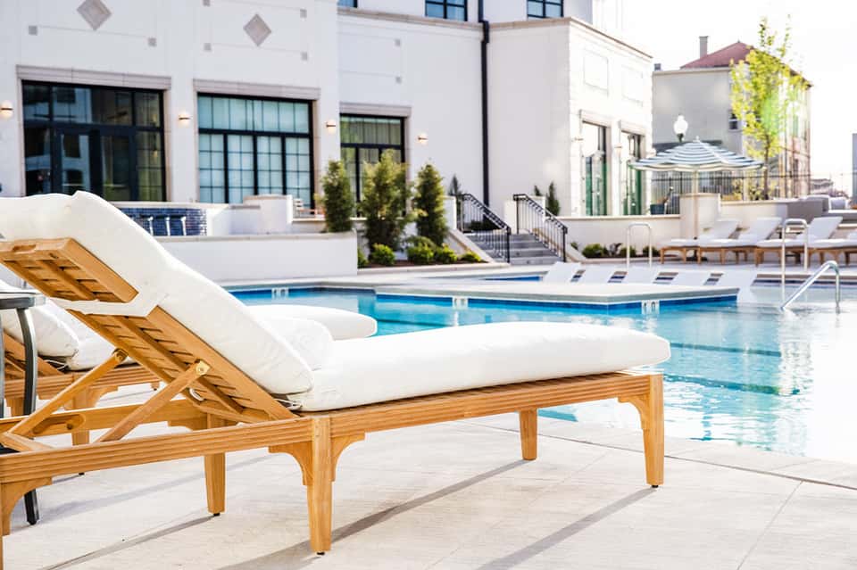 Modern resort pool with white wooden lounge chair, clean water, and contemporary white buildings