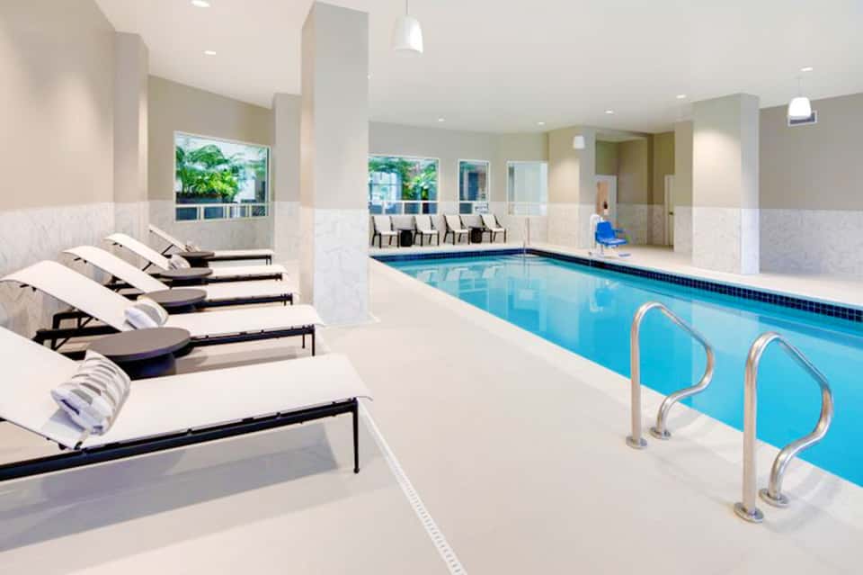 Indoor heated swimming pool with lounge chairs, white columns, and natural lighting
