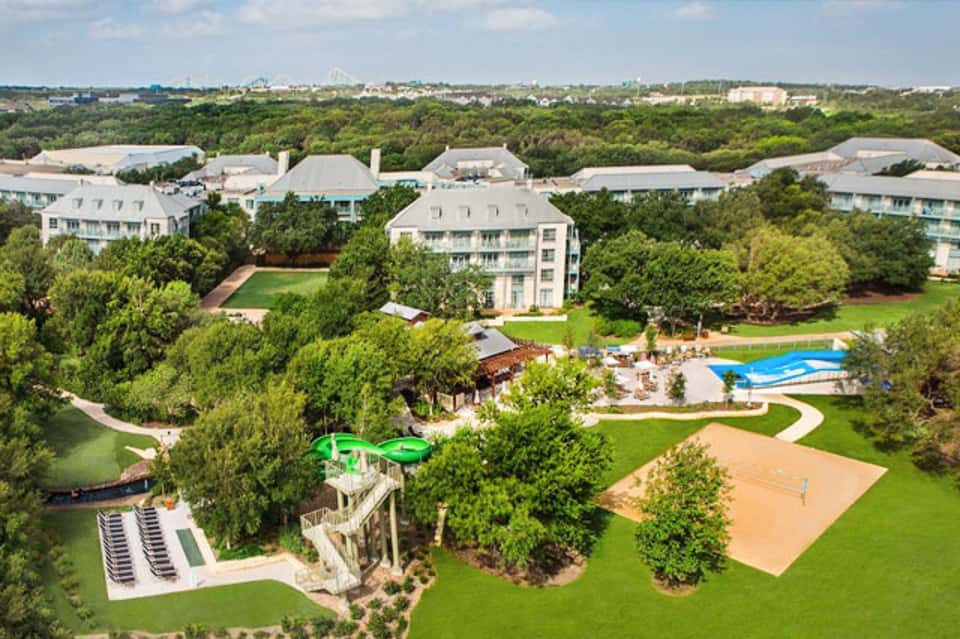 Aerial view of luxury resort with swimming pool, sports courts, and manicured grounds surrounded by trees