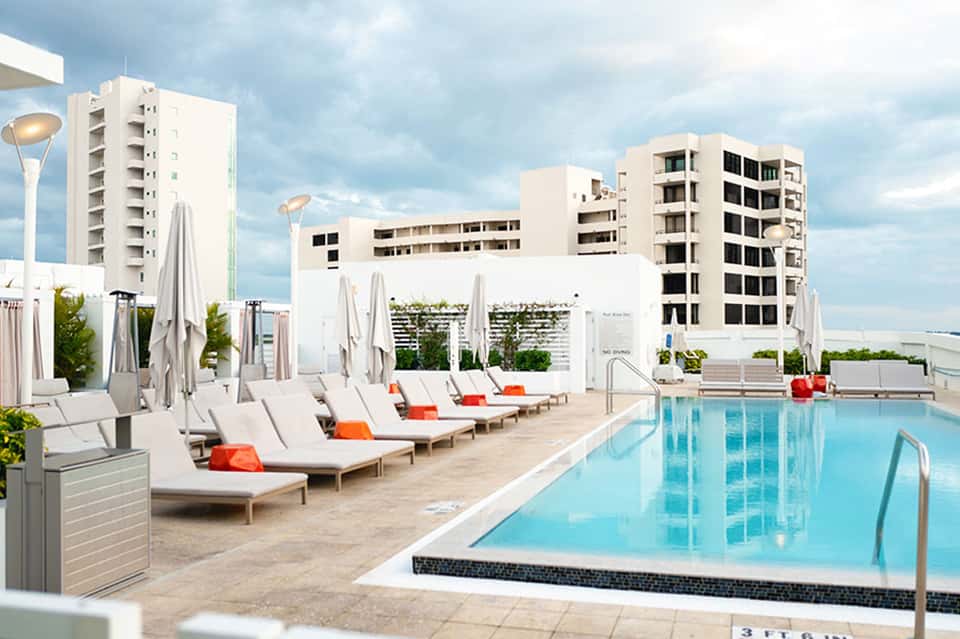 Modern rooftop pool deck with lounge chairs, umbrellas, and residential towers