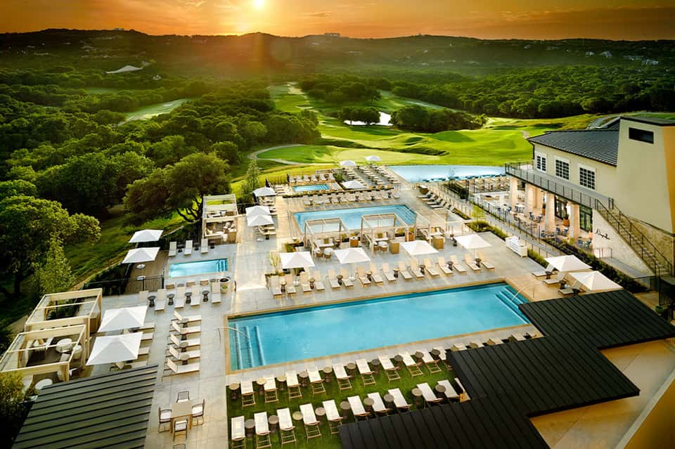 Aerial view of resort pools, loungers, and golf course with lush green landscape at sunset