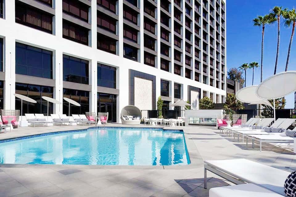 Modern hotel pool with pink lounge chairs, white umbrellas, and contemporary glass building facade