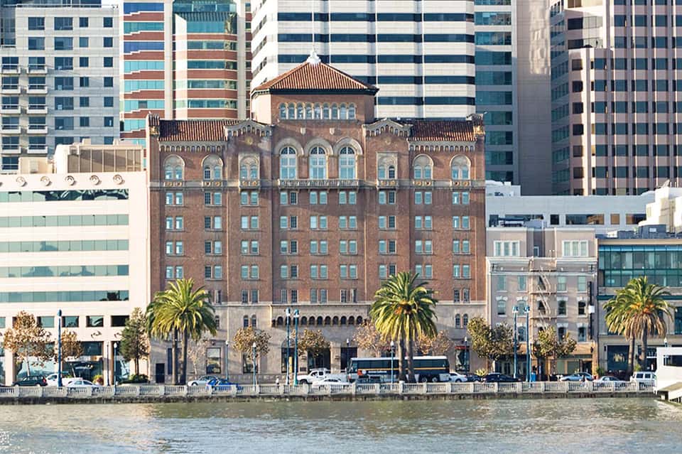 Historic brick building with arched windows on waterfront surrounded by modern skyscrapers